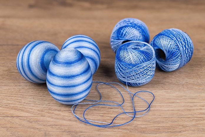 Blue colored striped Easter eggs and cotton yarn in decorative skeins on wooden background