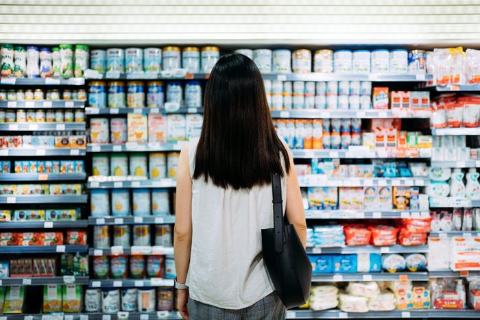 Rear View Of Young Asian Mother Groceries Shopping For Baby Products In A Supermarket. She Is Standing In Front Of The Baby Product Aisle And Have No Idea Which Product To Choose From