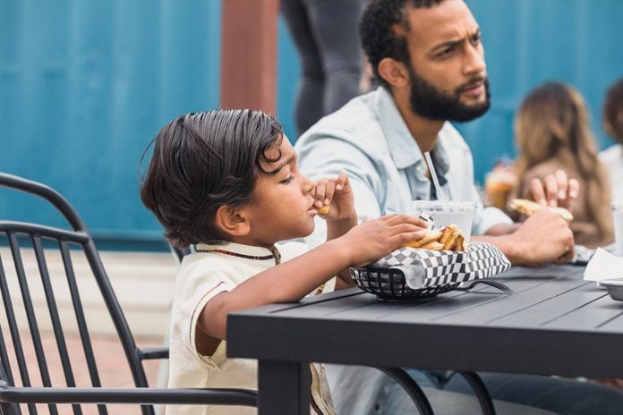 Boy eats food while dad chats at patio restaurant