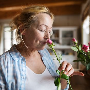 Senior woman in her kitchen smelling fragrance of pink rose
