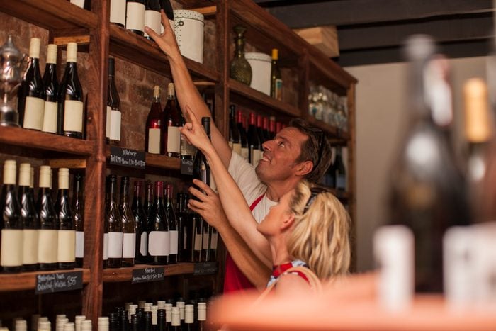 Man in wine shop helping customer reach wine bottle on top shelf