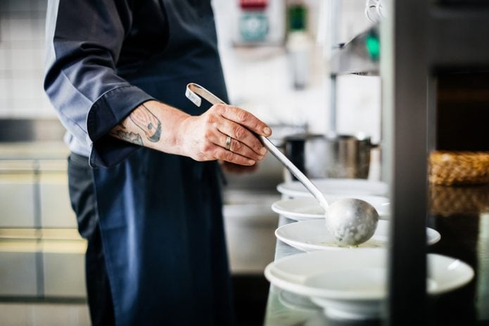 Chef With Tattoos Ladling Soup Into Bowls