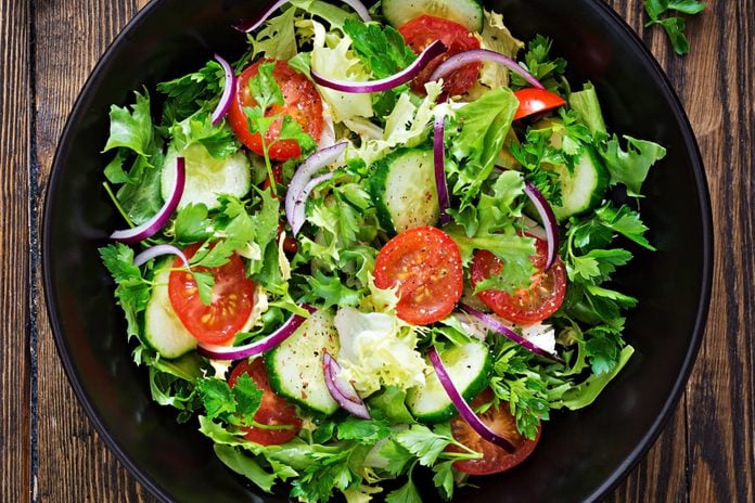 Salad from tomatoes, cucumber, red onions and lettuce leaves. Healthy summer vitamin menu. Vegan vegetable food. Vegetarian dinner table. Top view. Flat lay