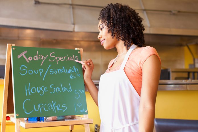 African American business owner writing cafe specials on blackboard