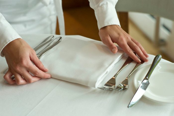 Waitress adjusting table settings in restaurant, mid section