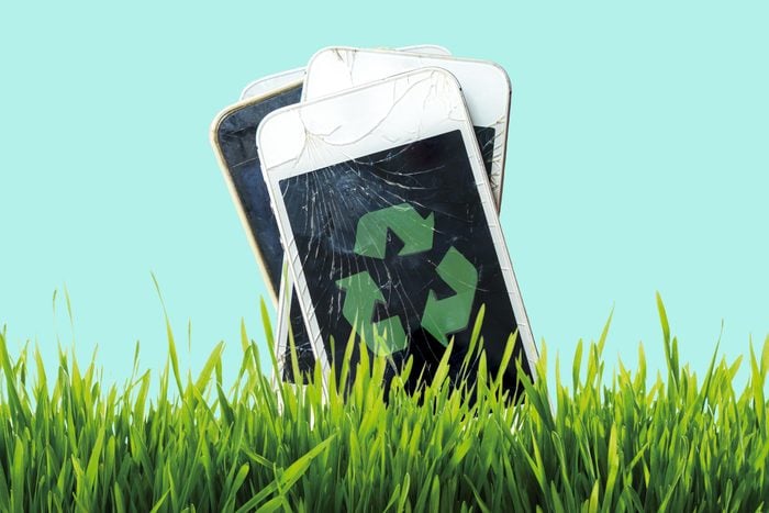old broken smart phones with a recycle symbol with green grass in the front and a blue background