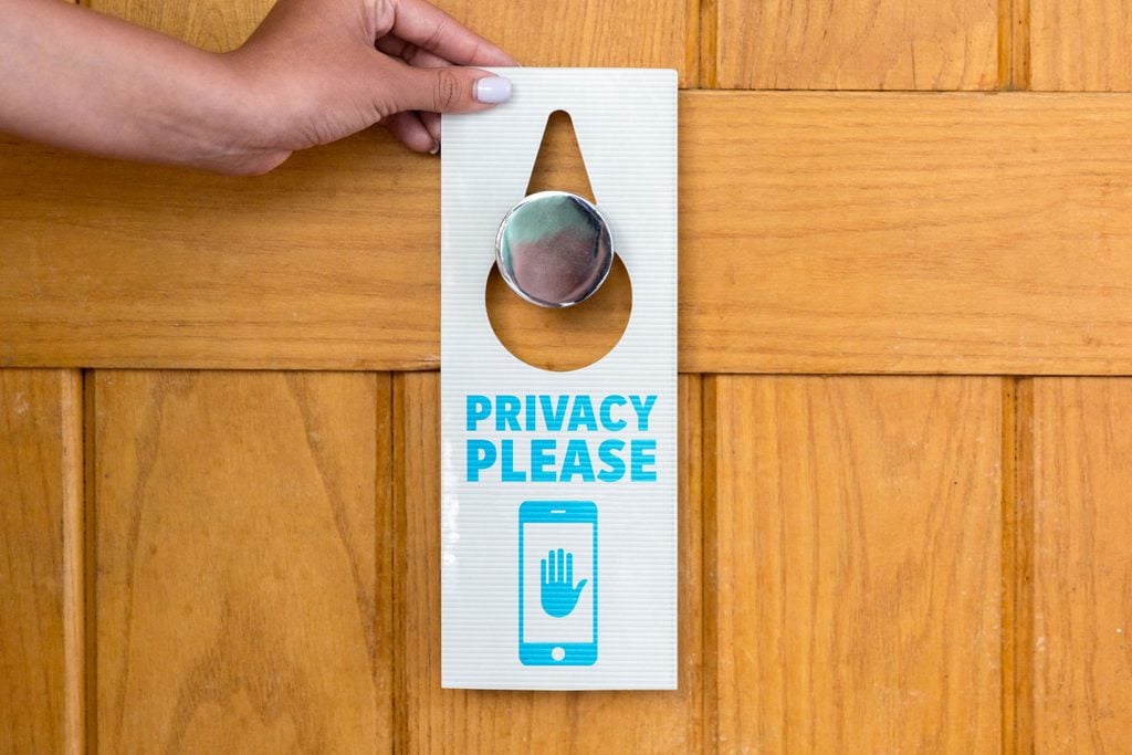 Hotel door hanger that says "privacy please" and shows a phone symbol with hand in the middle. The image represents privacy settings on a phone