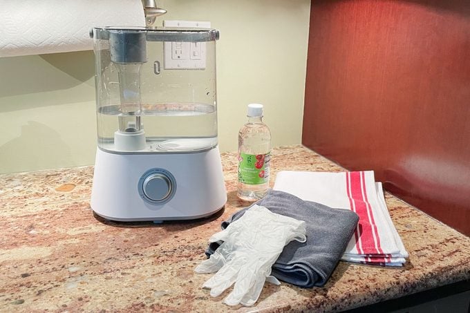 humidifier on kitchen counter next to cleaning supplies; vinegar, towel, gloves