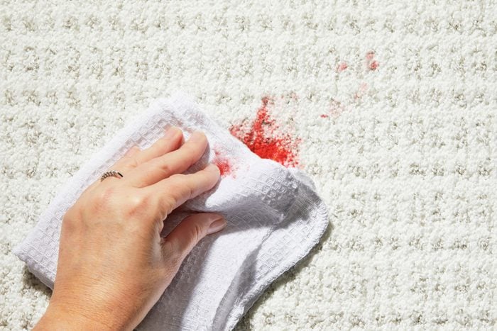 Hand using white cleaning cloth to blot blood stain on a white textured carpet