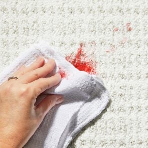 Hand using white cleaning cloth to blot blood stain on a white textured carpet
