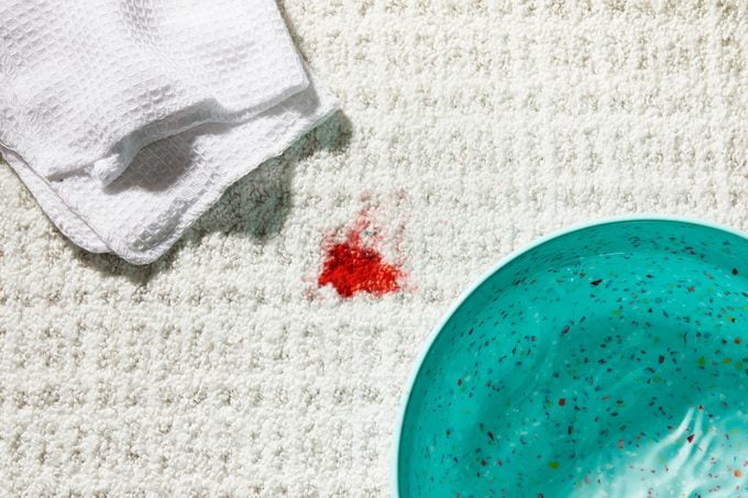 Blood stain on a white carpet with a bowl of warm water and white cleaning cloth nearby