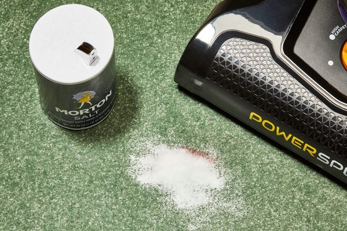 Salt covering a blood stain on a green carpet with vacuum cleaner nearby