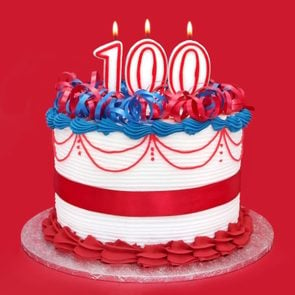 red, white, and blue cake with three numeral candles to show 100, on vibrant red background
