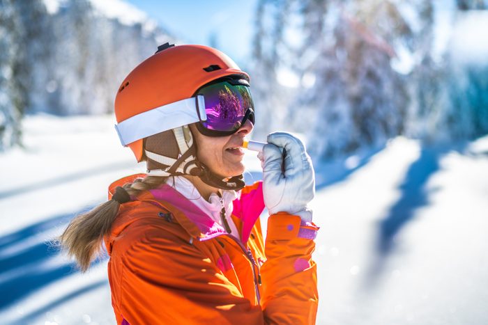 skier woman with skiing helmet putting on sunscreen lip protection