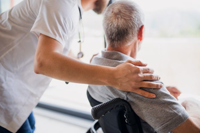 A midsection of male healthcare worker talking to senior man in wheelchair indoors at home.