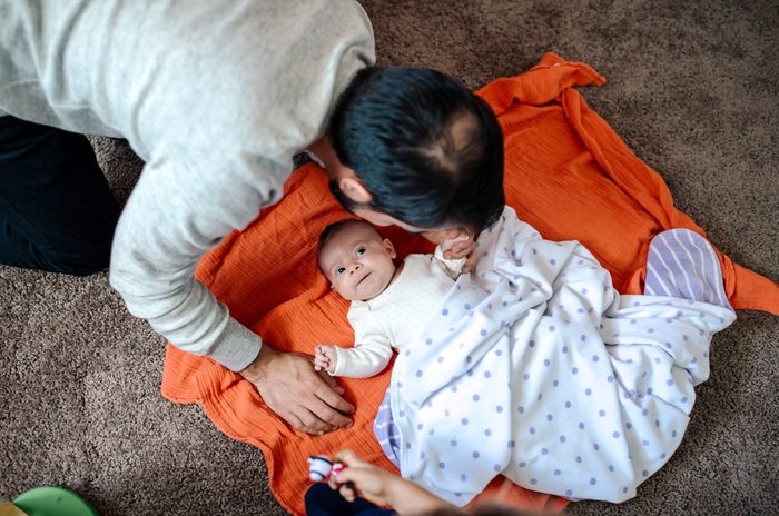 Father leaning over baby on orange blanket on floor