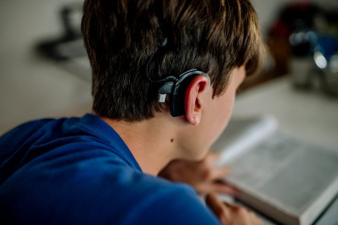 Rear view of teenage boy with cochlear implant doing homework