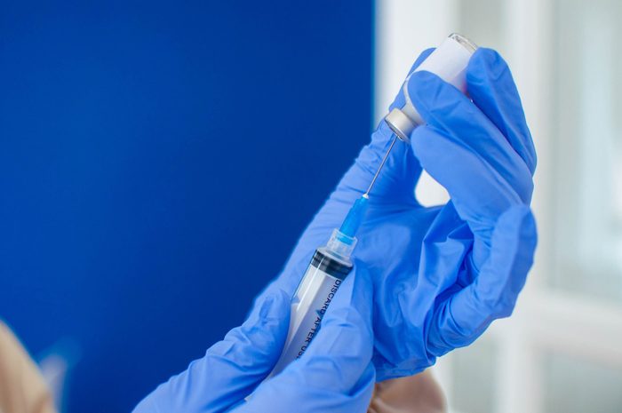 close up of a Doctor In Blue Protective Gloves Holding A Medical Syringe And Vial of the covid-19 vaccine