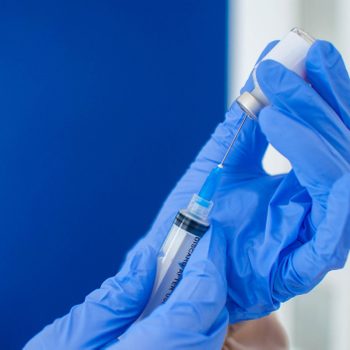 close up of a Doctor In Blue Protective Gloves Holding A Medical Syringe And Vial of the covid-19 vaccine