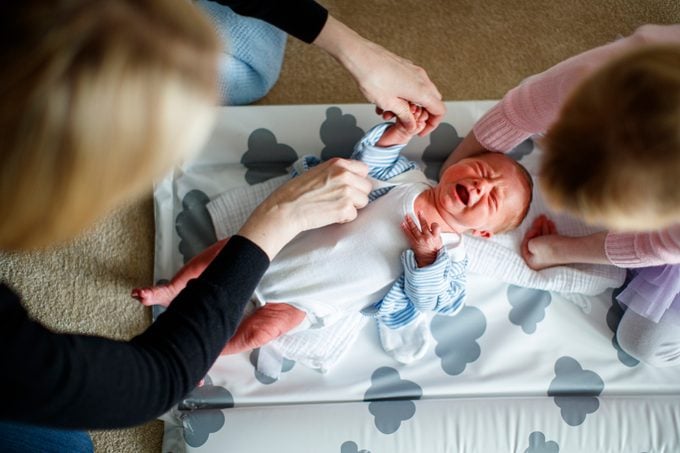 Mother and daughter tending to crying baby on changing mat