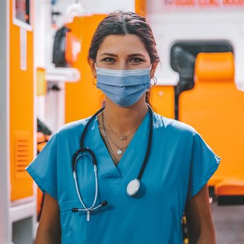 Portrait of young female paramedic with face mask working in an ambulance during pandemic