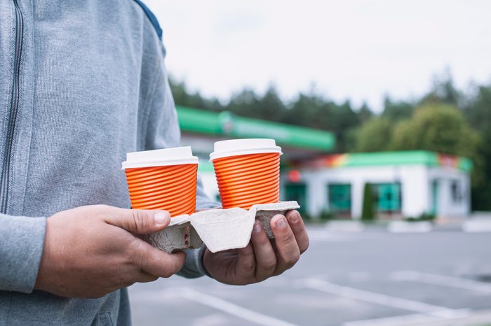 A man holds two cups of coffee in his hands at a gas station.