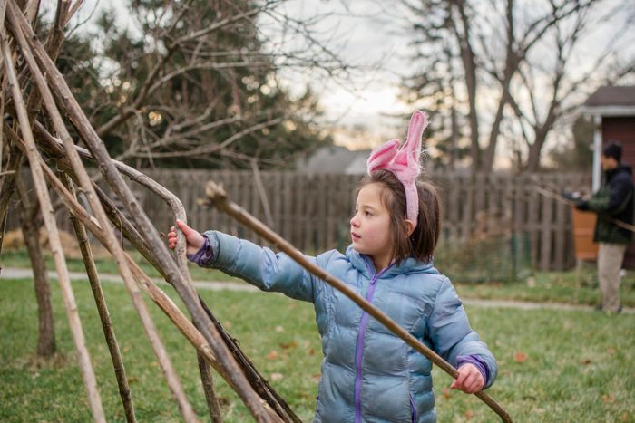 A little girl in bunny ears and jacket builds fort with father in yard
