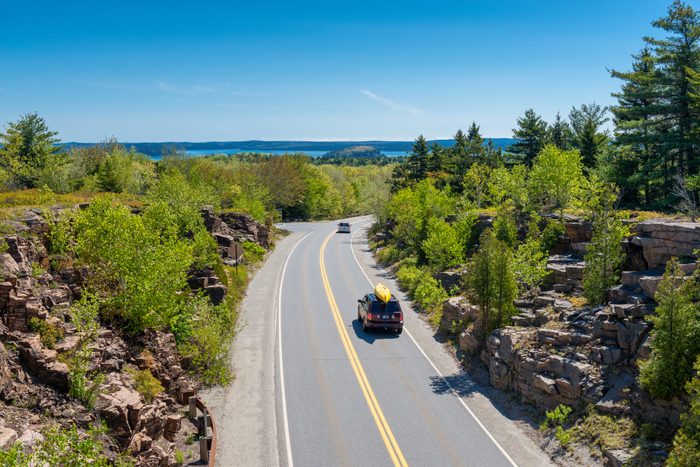 Cars driving on road in Acadia National Park, Maine, USA. One car holds a canoe on its roof.