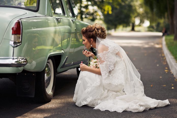 Side View Of Bride Applying Lipstick By using a car as mirror