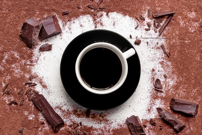mug of brewed cacao surrounded by ground cacao and chunks of chocolate