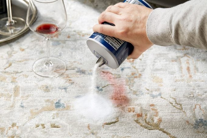 hand pouring salt on a red wine stain on a rug