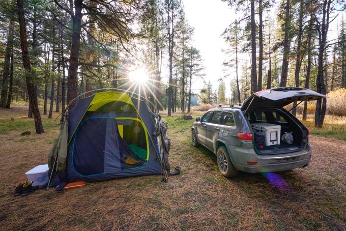 Vehicle Parked next to a Tent In Campground with the setting sun shining through the trees