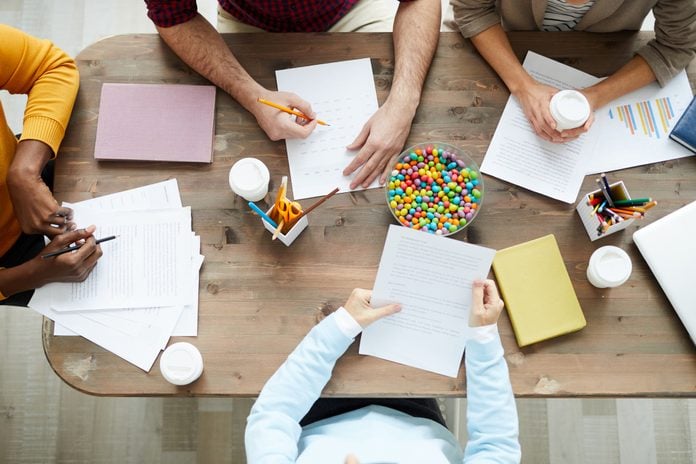 Directly above view of marketing specialists sitting at wooden table with papers and candies and discussing reports and charts