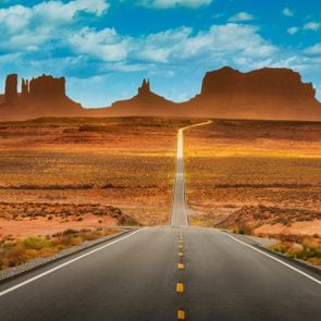 View of historic U.S. Route 163 running through famous Monument Valley in beautiful golden evening light at sunset on a beautiful sunny day with blue sky in summer, Utah, USA