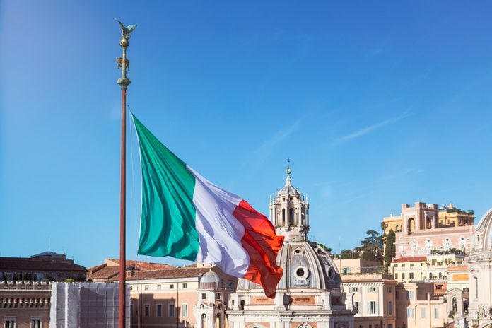 Italy, Rome, Italian flag fluttering against clear blue sky and dome of Santa Maria di Loreto
