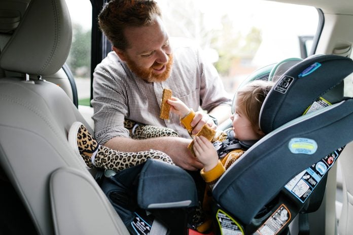 Father buckling daughter (2-3) in car seat