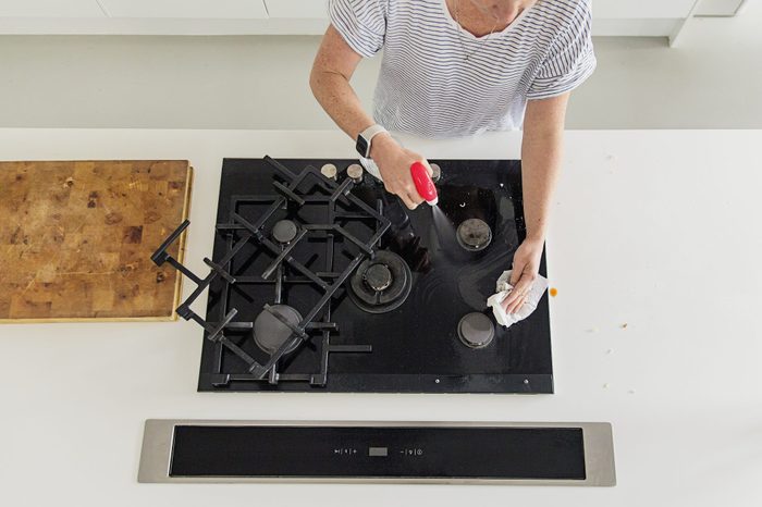woman degreasing a black gas stovetop, viewed from overhead