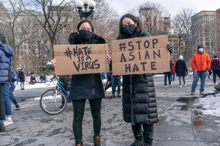 two women at a rally to support the Asian community hold signs reading "#hate is a virus" and "#stop asian hate" in Washington Square Park, New York City