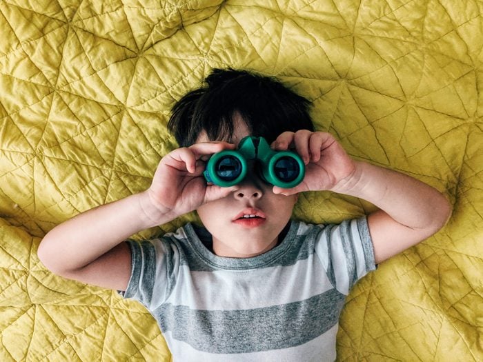 A child looks through binoculars while laying on a bed.