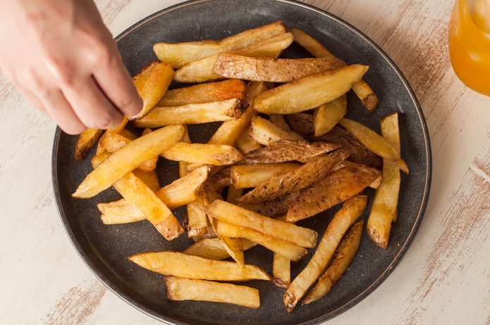 Seasoning a fresh home made fried french fries on a rustic white dining table