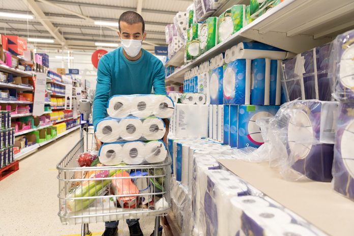 Man buying toilet paper at supermarket and wearing a face mask during coronavirus pandemic