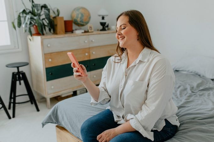 Happy Plus Size Woman Using her Smartphone in Bedroom
