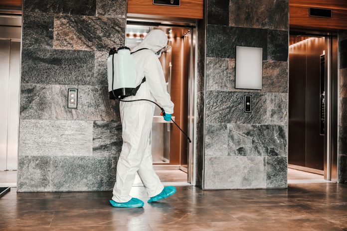 person spraying disinfectant around the elevator in the lobby of a hotel