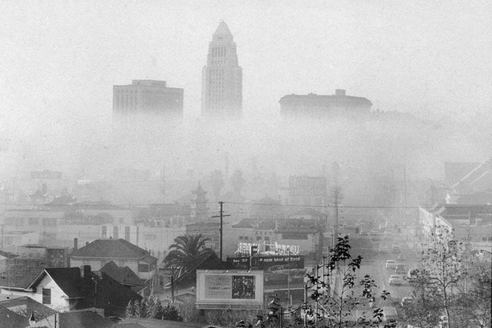 the skyline of downtown Los Angeles including the city hall (center) and the United States Courthouse (left), and Hall of Justice (right) shrouded and obscured by smog, a form of industrial and automotive air pollution particularly problematic in the area during the mid 20th Century, 1956.