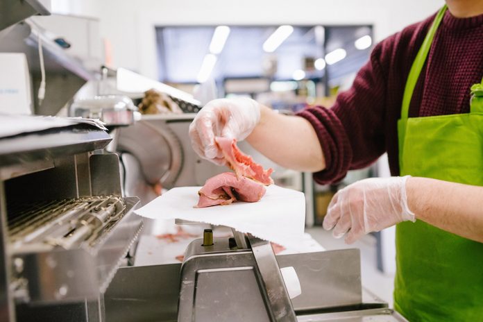 Employee in general store weighing sliced meat in kitchen