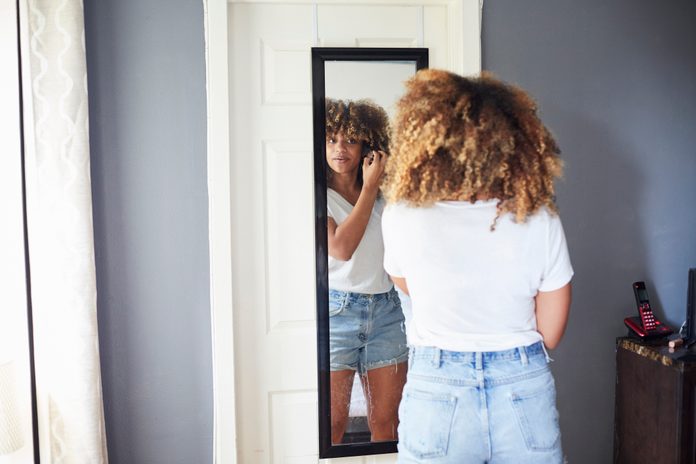 Black woman examining hair in mirror