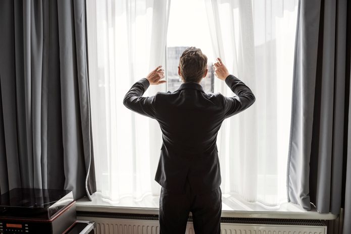 Rear view of businessman opening white curtain on window in hotel room