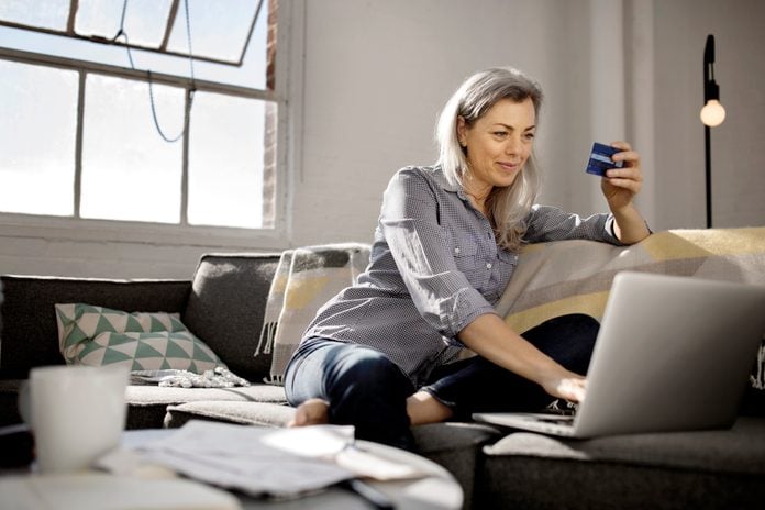 Mature woman holding debit card while using laptop on sofa