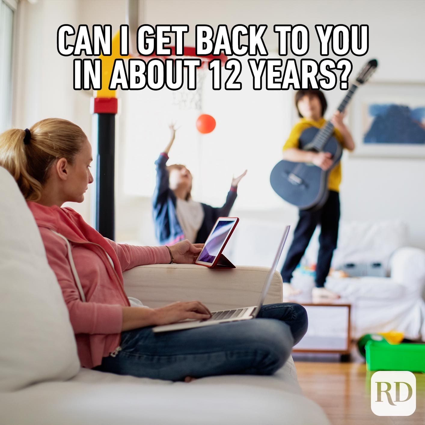 Mother on laptop while children play electric guitar and basketball behind her. MEME TEXT: Can I get back to you in about 12 years?