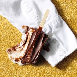 Chocolate popsicle melting to create a stain on a shirt sleeve and yellow carpet background